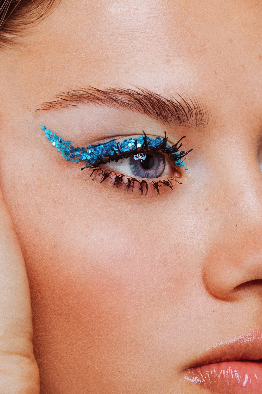 A woman wearing blue eye shadow and lip gloss looks into the camera