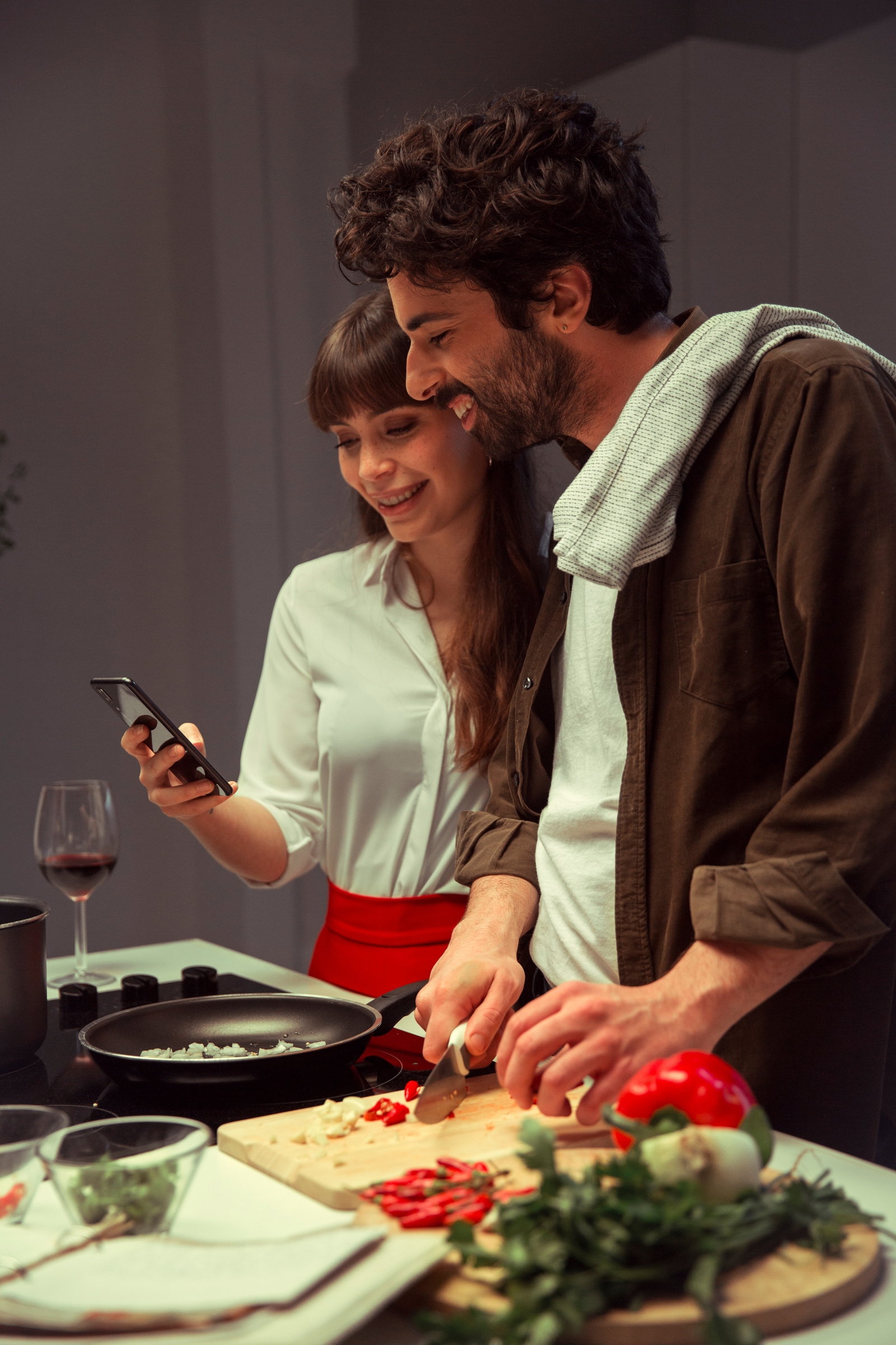 2 people in kitchen, one using a cell phone and the other smiling