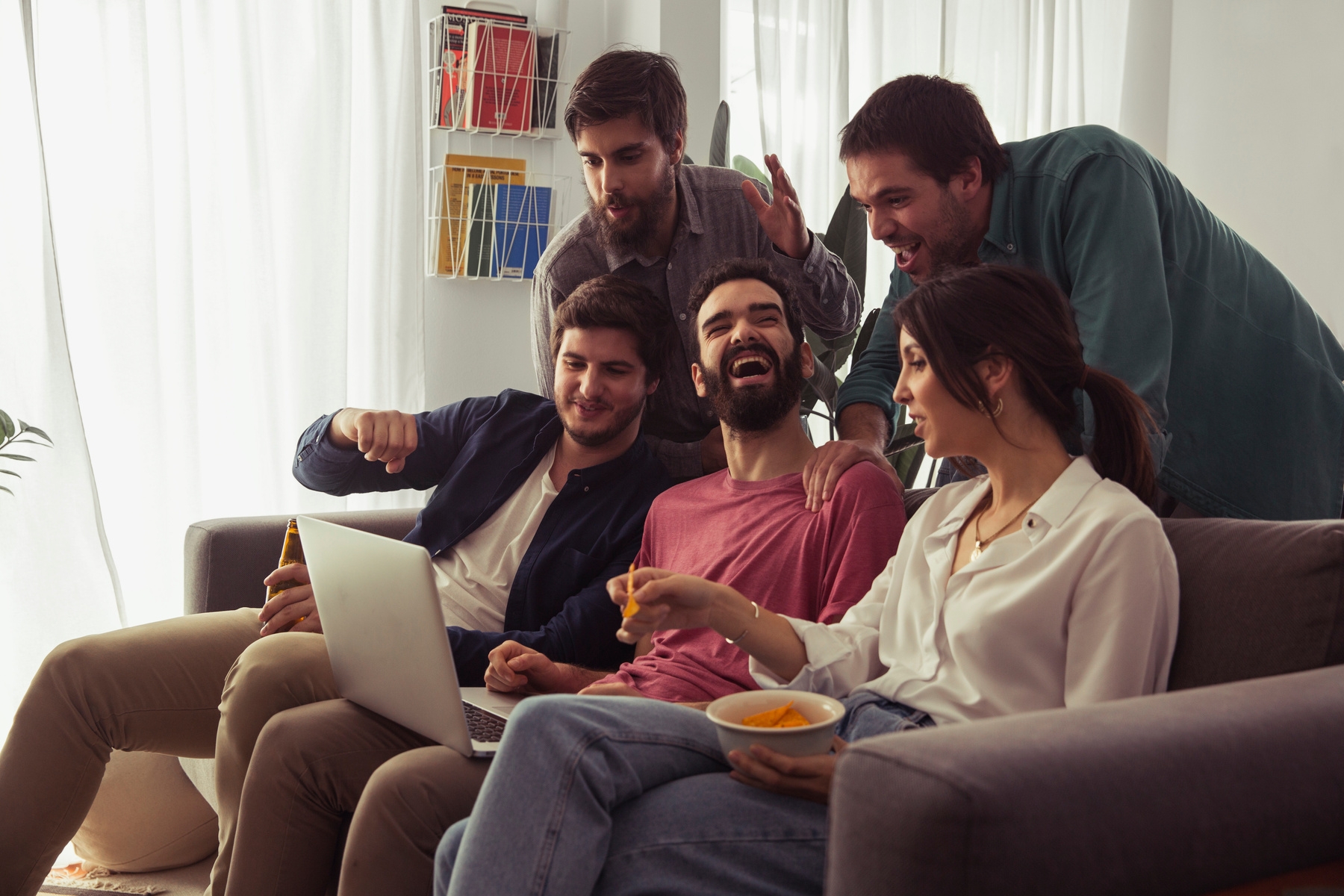 6 people are gathered around a couch, holding drinks and engaging in conversation. One person is holding a bowl of
popcorn