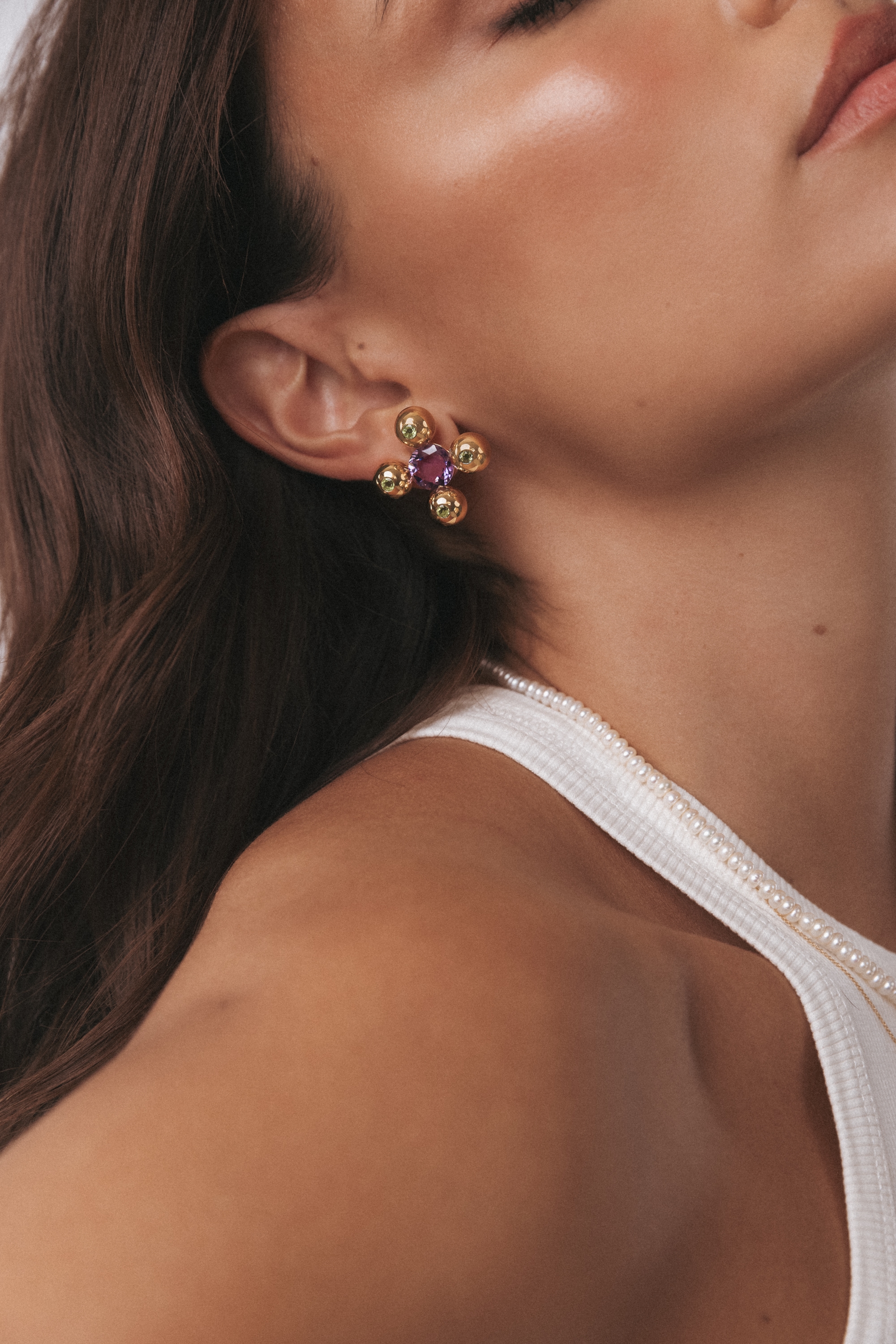 A woman with a white tank top and gold earrings poses for the camera