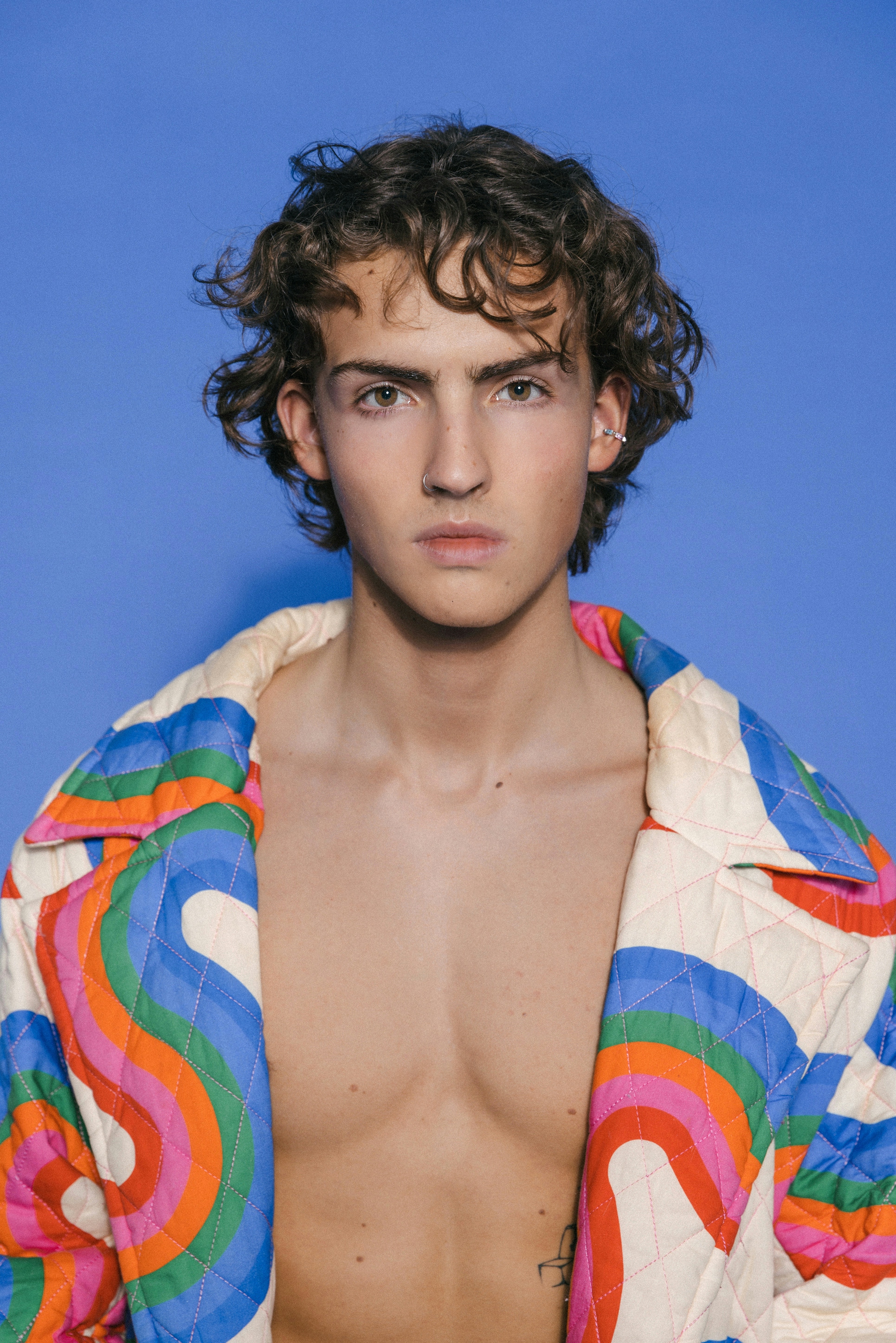 A young man wearing a colorful, patterned shirt and no undershirt
