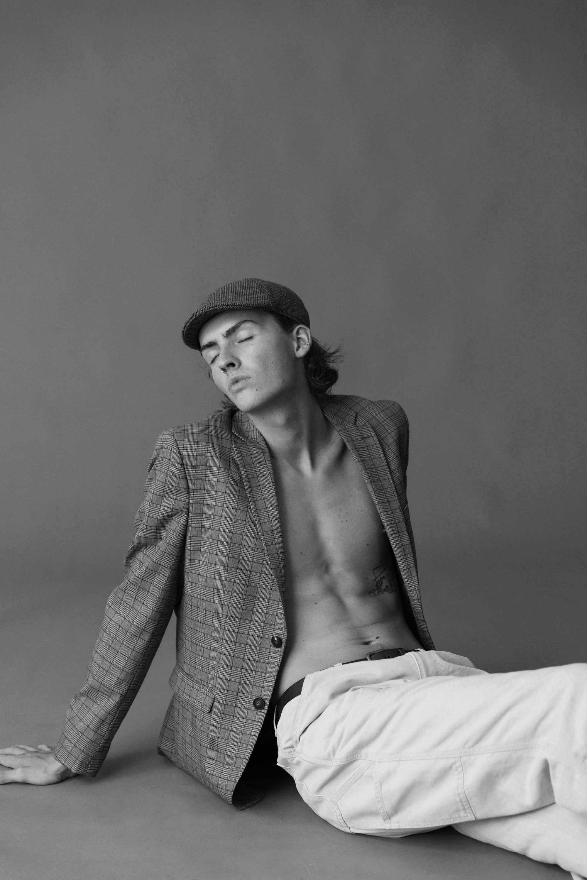 20-something shirtless man in a hat, lying on the floor with his jacket over him