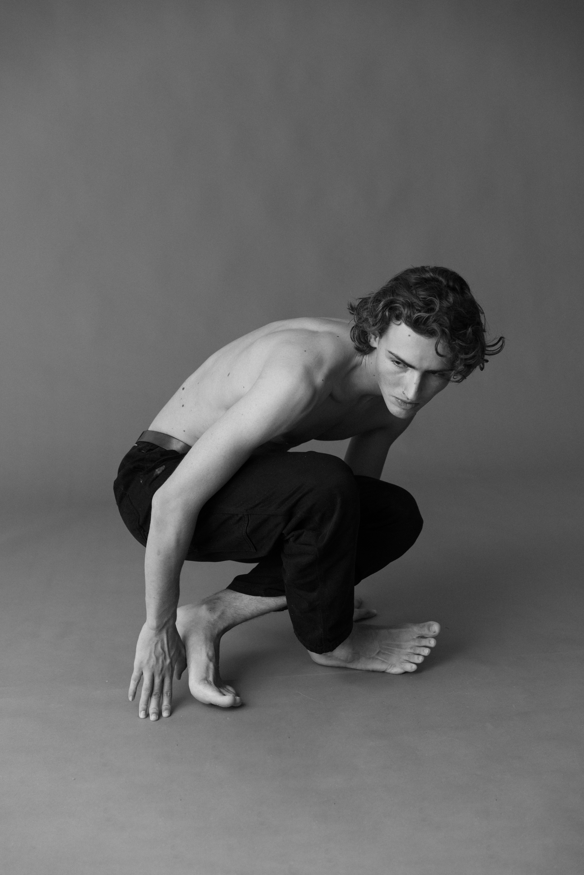 A young man in black pants and shirt with a tattoo kneeling down on the ground