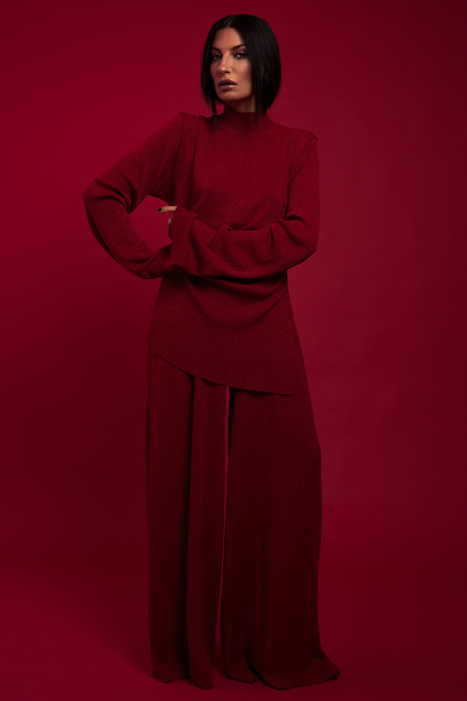 A woman in a red dress and red pants standing on a red background
