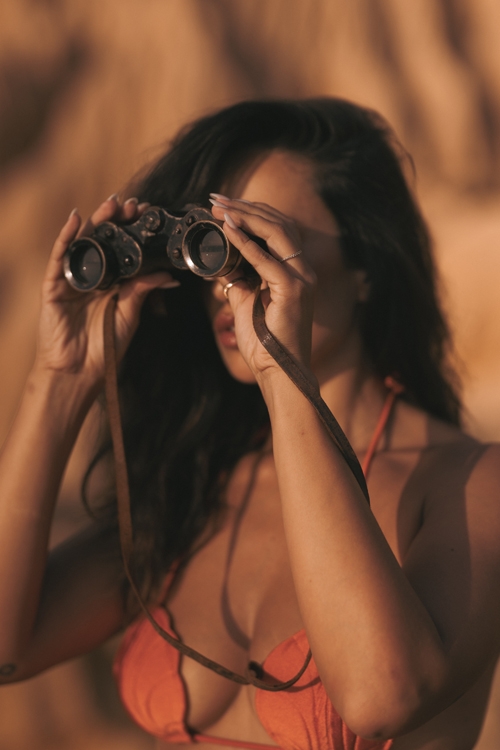 Young woman wearing orange bikini top, looking at camera with her binoculars