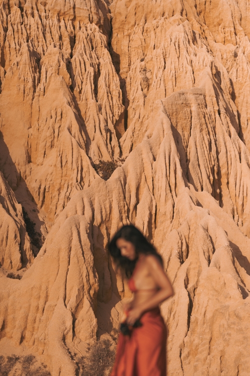 The image features a beautiful woman walking through a red dirt canyon, surrounded by an impressive array of rock formations