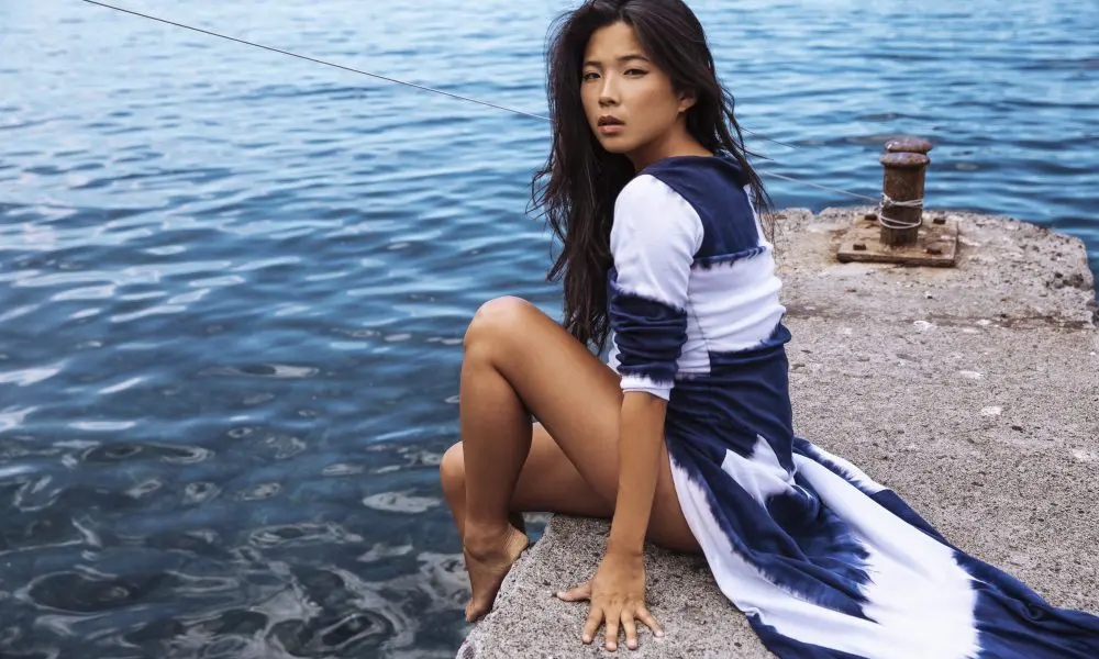 Jani Zhao with dark hair is sitting near to the ocean, capturing a relaxing and beautiful moment by the water. Photo by KAT V Photography, Magazine: LuxWOMAN.