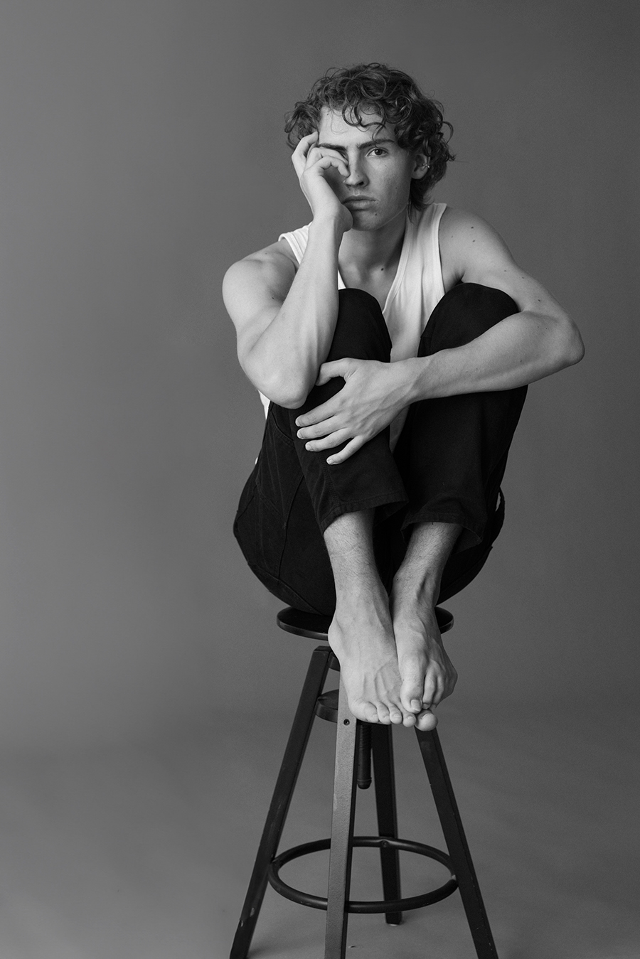 A man in a white shirt and jeans sits on a barstool