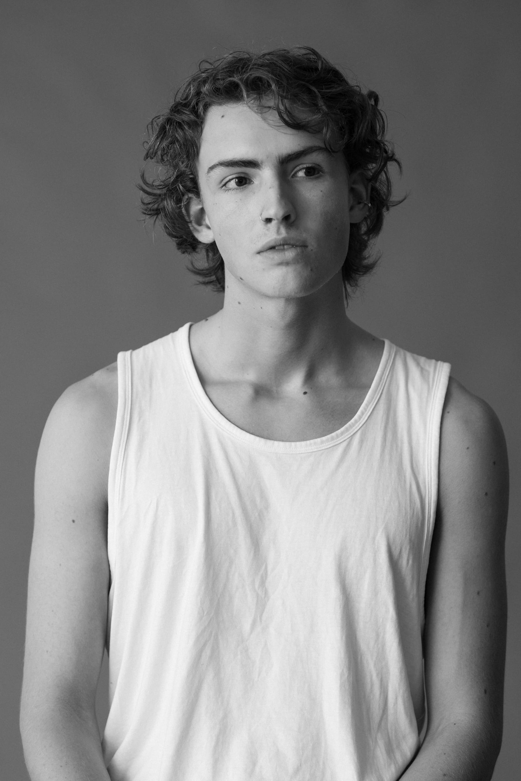 Young man with wavy hair in white tank top, black-and-white photo with dark background