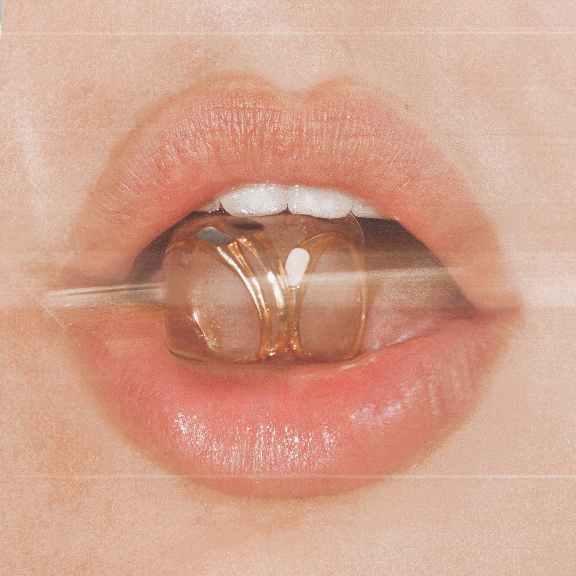 The image is a close-up of a woman's mouth, with a gold grill on her teeth. Her lips are parted, and her tongue is visible. The background is out of focus.