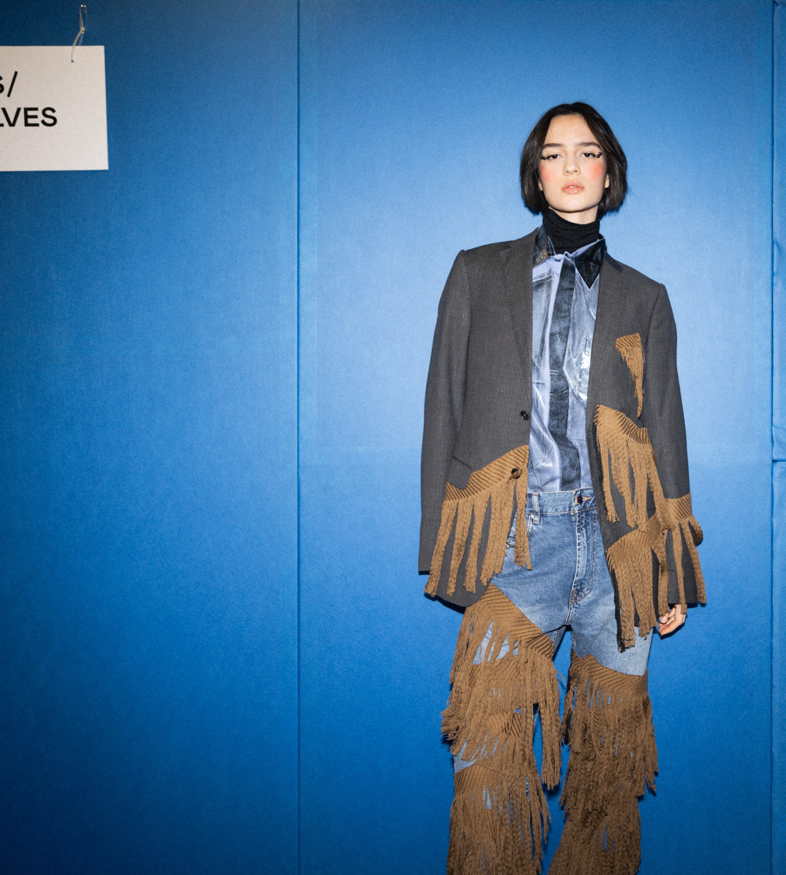 Asian woman in fringe blazer, blue shirt, jeans, and boots, showcasing chic street style.