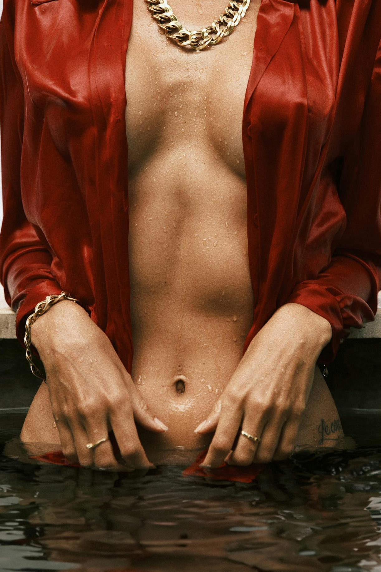 A naked woman in a red robe stands in the water. She is wearing gold and silver
jewelry, including bracelets on her wrists